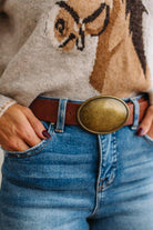 Close up image of a woman in blue jeans and patterned sweater featuring a Western Oval Buckle Leather Belt.