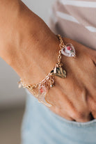 GOLD CHARM BRACELET WITH WESTERN INSPIRED METALLIC AND PINK OR CLEAR ACRYLIC CHARMS.