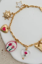 GOLD CHARM BRACELET WITH WESTERN INSPIRED METALLIC AND PINK OR CLEAR ACRYLIC CHARMS.