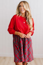 Blonde woman wearing a knee length dress with red french terry top, and red plaid skirt bottom with pockets on the sides.