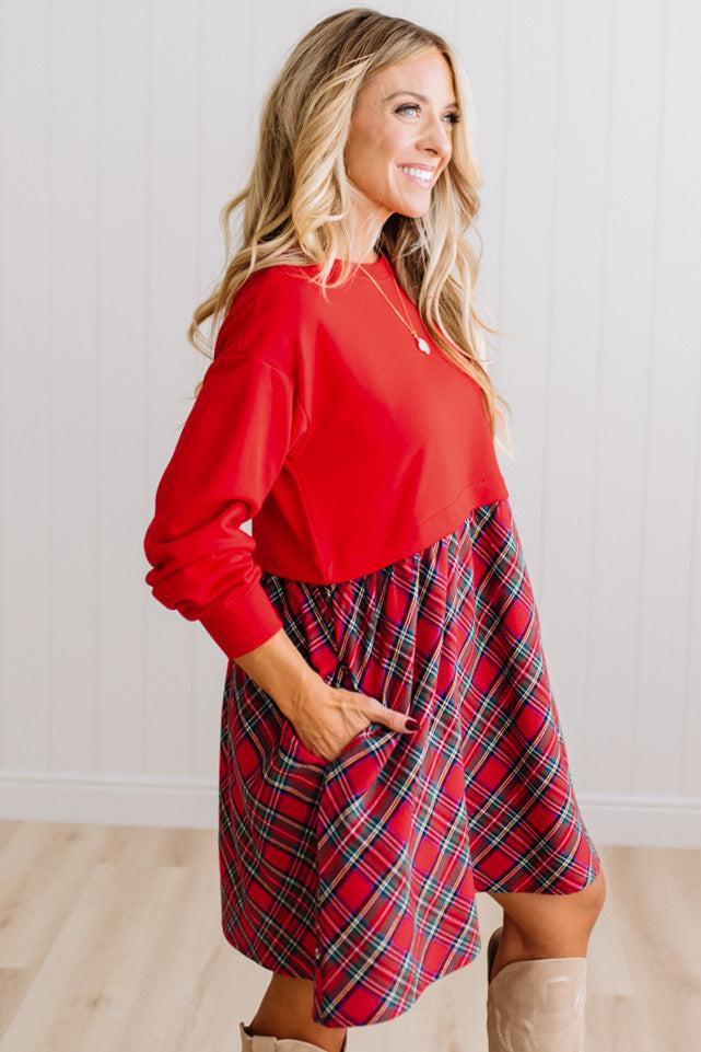 Blonde woman wearing a knee length dress with red french terry top, and red plaid skirt bottom with pockets on the sides.