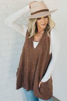 BLONDE WOMAN WEARING AN OVERSIZED V-NECK LONG SOFT SWEATER VEST WITH SIDE POCKETS.