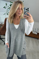 BLONDE WOMAN WEARING AN OVERSIZED V-NECK LONG SOFT SWEATER VEST WITH SIDE POCKETS.