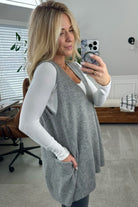 BLONDE WOMAN WEARING AN OVERSIZED V-NECK LONG SOFT SWEATER VEST WITH SIDE POCKETS.