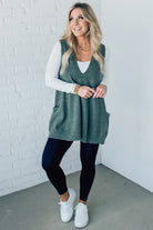 BLONDE WOMAN WEARING AN OVERSIZED V-NECK LONG SOFT SWEATER VEST WITH SIDE POCKETS.