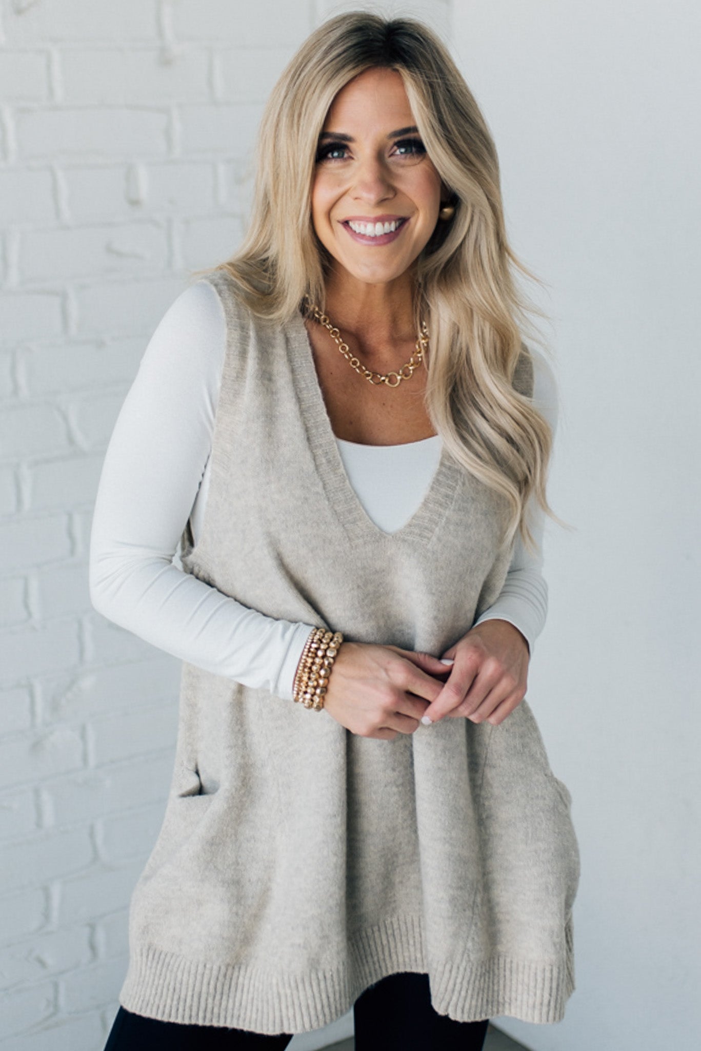 BLONDE WOMAN WEARING AN OVERSIZED V-NECK LONG SOFT SWEATER VEST WITH SIDE POCKETS.