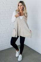 BLONDE WOMAN WEARING AN OVERSIZED V-NECK LONG SOFT SWEATER VEST WITH SIDE POCKETS.