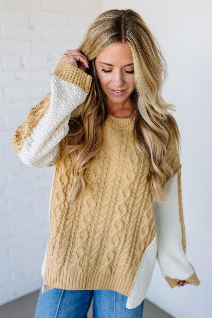 Woman wearing a beige cable knit sweater with white sleeves against a light background