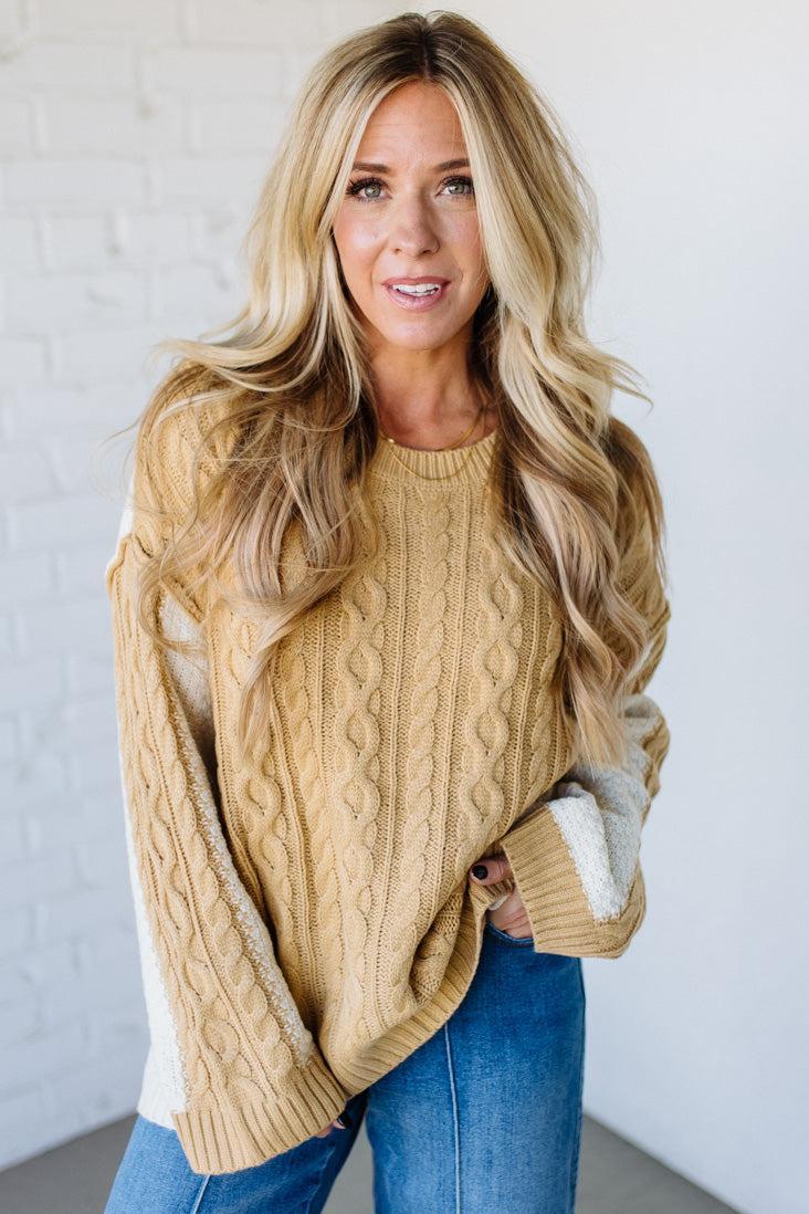 Woman wearing a beige cable knit sweater with white lining against a white background