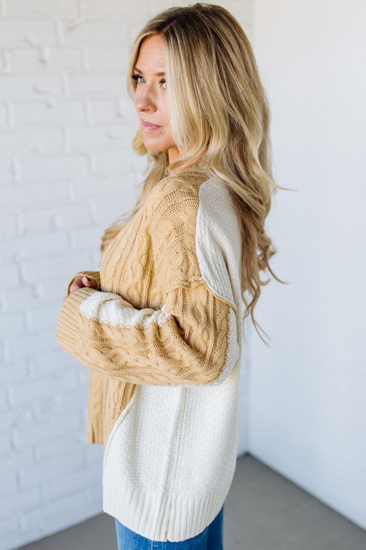 Woman wearing a beige and white cardigan against a white brick wall.