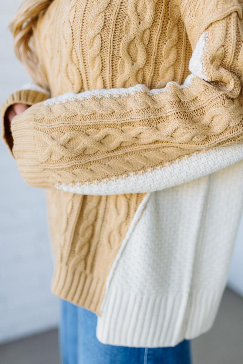 Close-up of a person wearing a beige cable knit sweater with white lining.