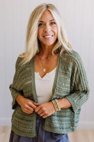 Woman wearing a green patterned cardigan over a white top with a neutral background