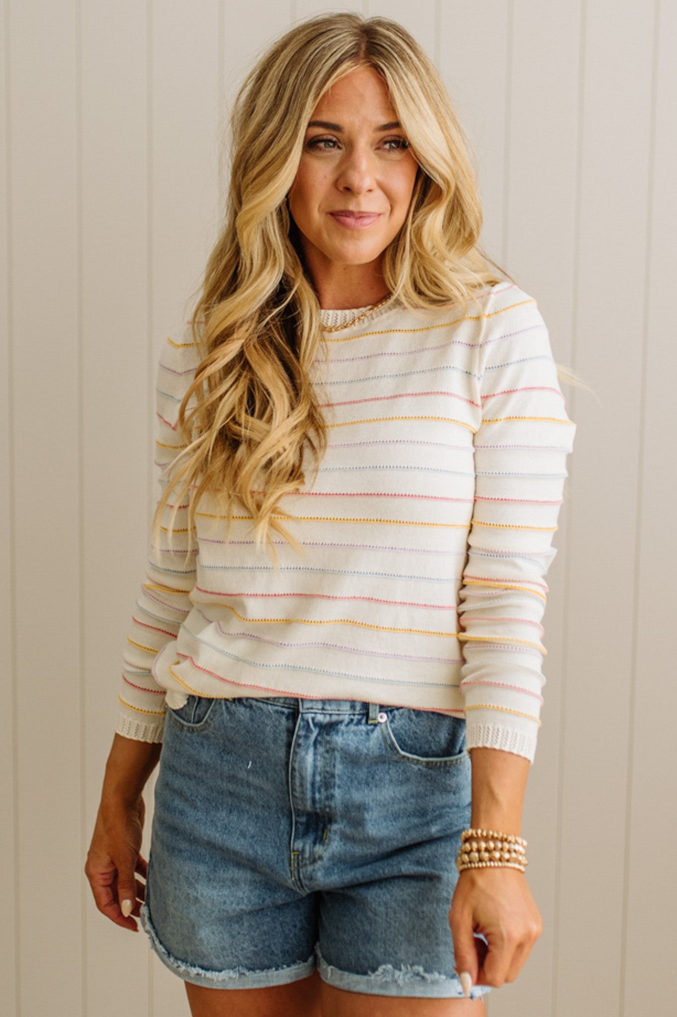 Woman wearing a striped sweater and denim shorts against a neutral background