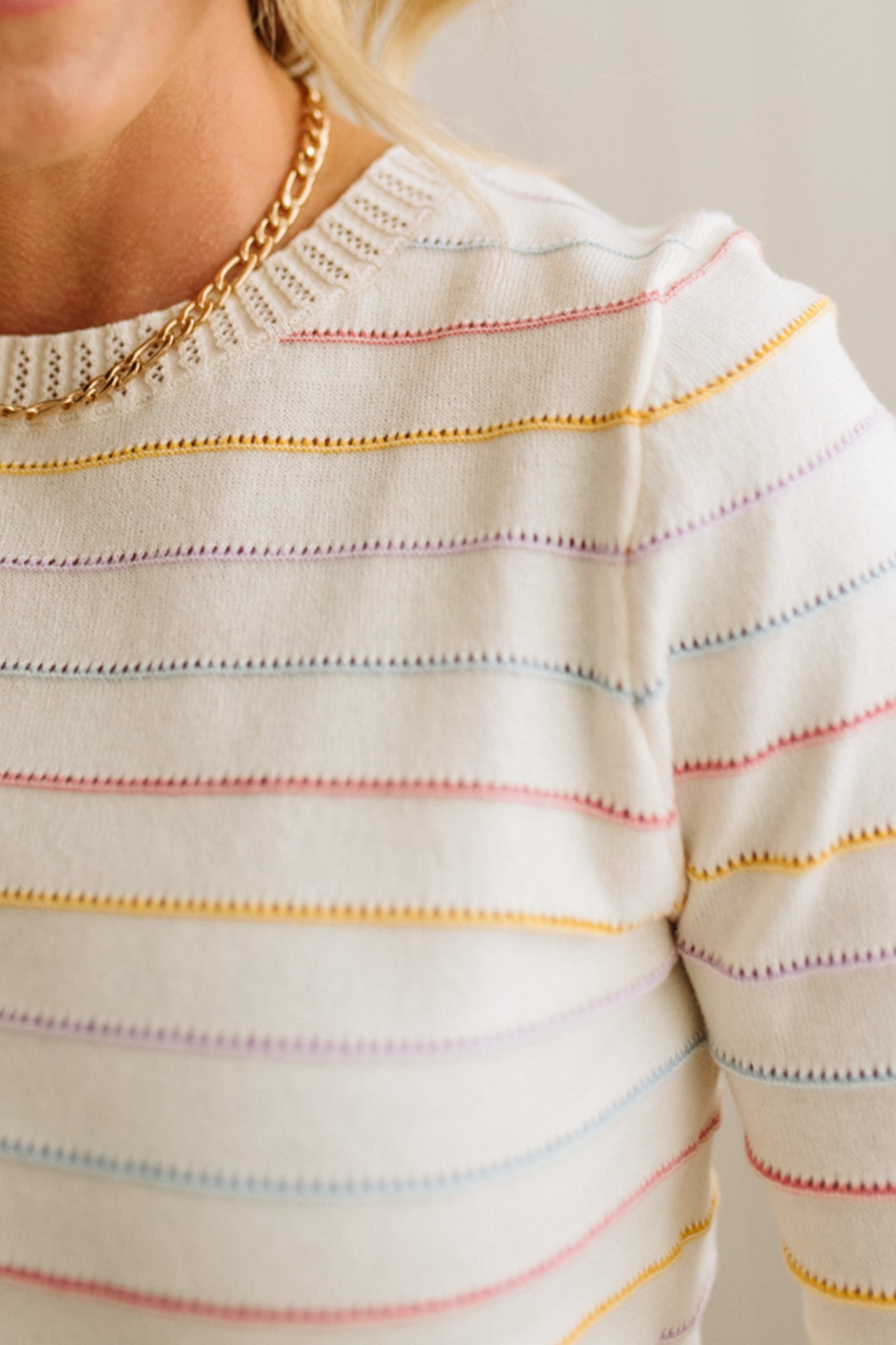 Close-up of a person wearing a white sweater with colorful stripes and a gold chain necklace.