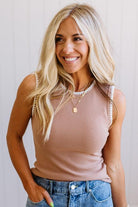 Woman wearing a beige tank top and blue jeans with a plain background