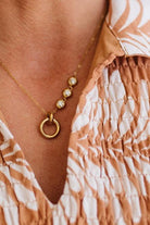 Gold necklace with circular pendant worn by a person in a patterned shirt.