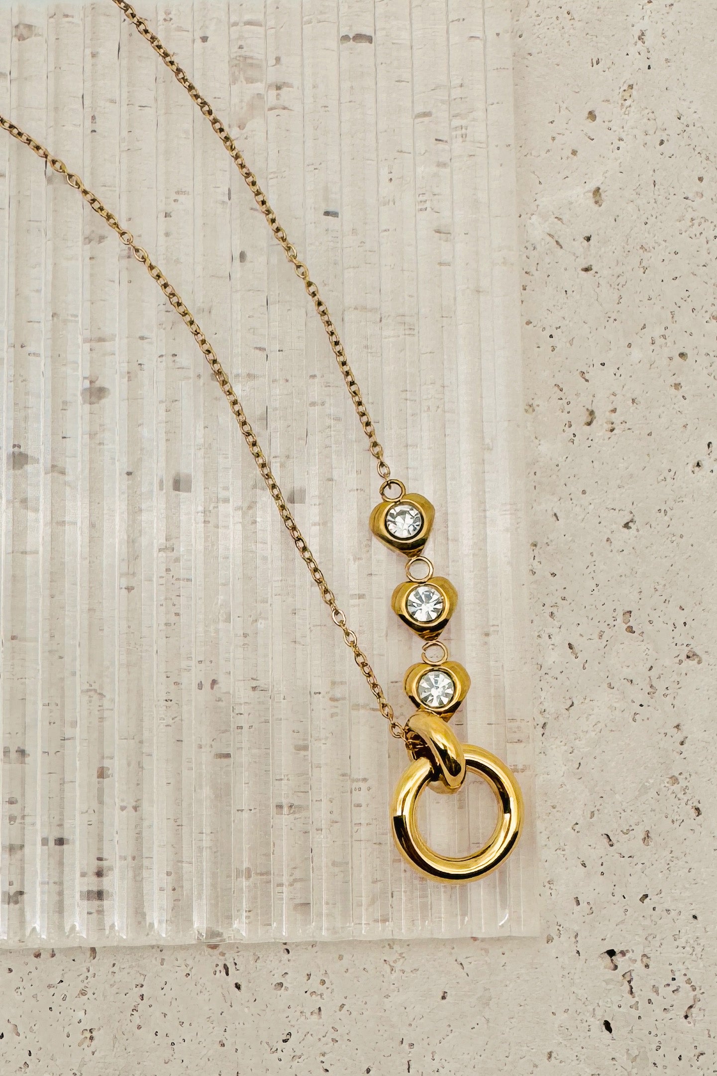Gold necklace with circular pendants on a textured beige surface