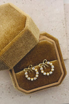 Gold hoop earrings with pearl accents on a brown velvet jewelry box.