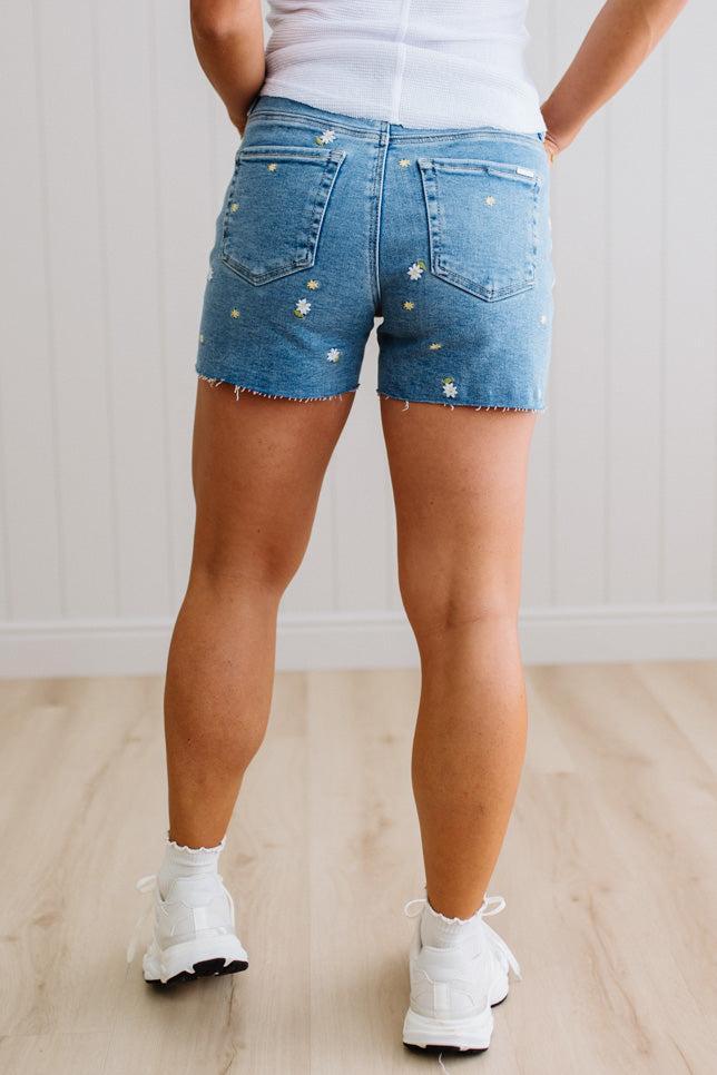 Person wearing blue denim shorts with white sneakers on a light wooden floor.