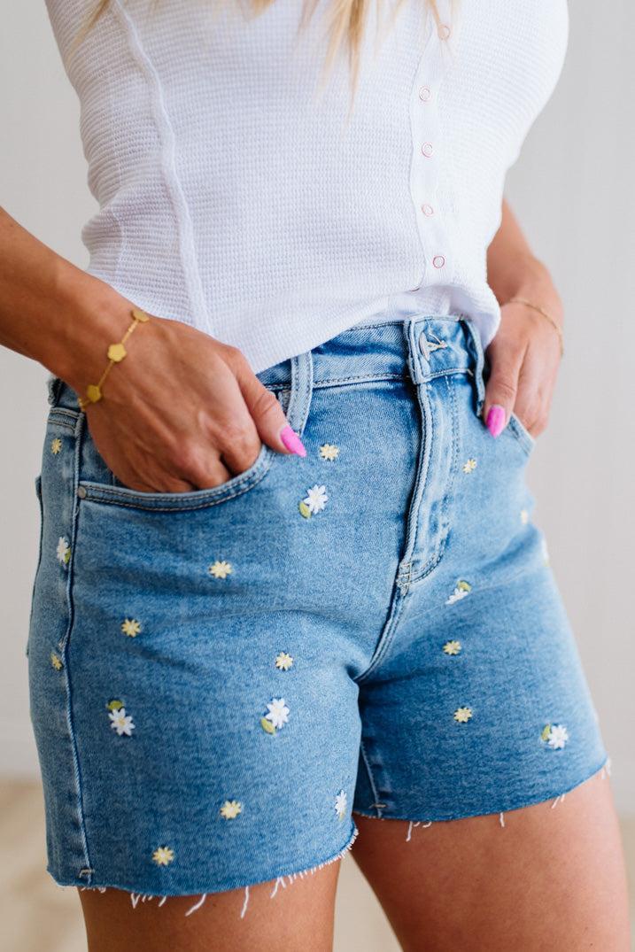 Person wearing blue denim shorts with floral embroidery and a white top.