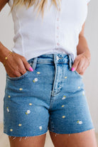 Person wearing blue denim shorts with floral embroidery and a white top.