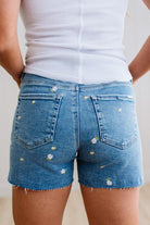 Blue denim shorts with floral embellishments worn by a person on a plain background
