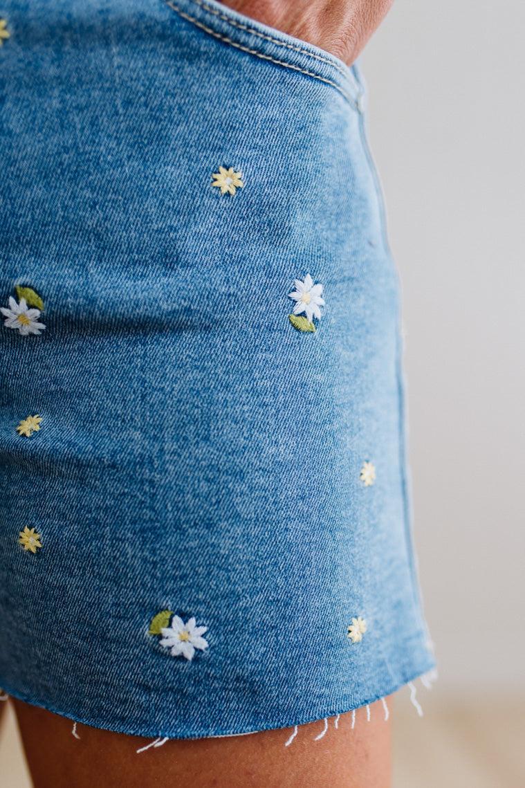 Blue denim skirt with floral embroidery on a neutral background