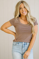 Woman wearing a brown ribbed t-shirt and blue jeans against a neutral background