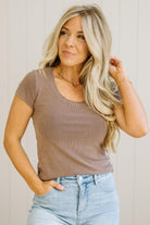 Woman wearing a brown ribbed top and light blue jeans against a neutral background