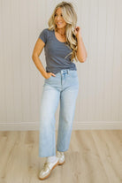 Woman wearing a gray t-shirt and light blue jeans standing against a white paneled wall.