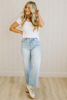 Woman wearing a white t-shirt and light blue jeans standing against a plain wall.