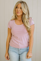 Woman wearing a pink top and light blue jeans against a neutral background