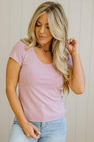 Woman wearing a light pink t-shirt and blue jeans against a neutral background