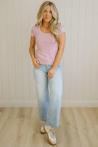 Woman wearing a pink top and light blue jeans standing against a white paneled wall.
