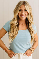 Woman wearing a blue ribbed top and light blue jeans against a neutral background