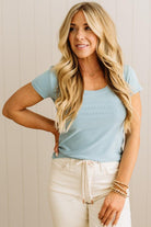 Woman wearing a blue ribbed top and light blue jeans against a neutral background