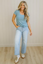 Woman wearing a blue t-shirt and jeans standing against a light-colored wall.