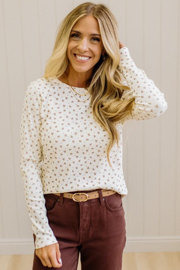 Blonde woman in brown jeans wearing a cream long sleeve tee with brown botanical print.