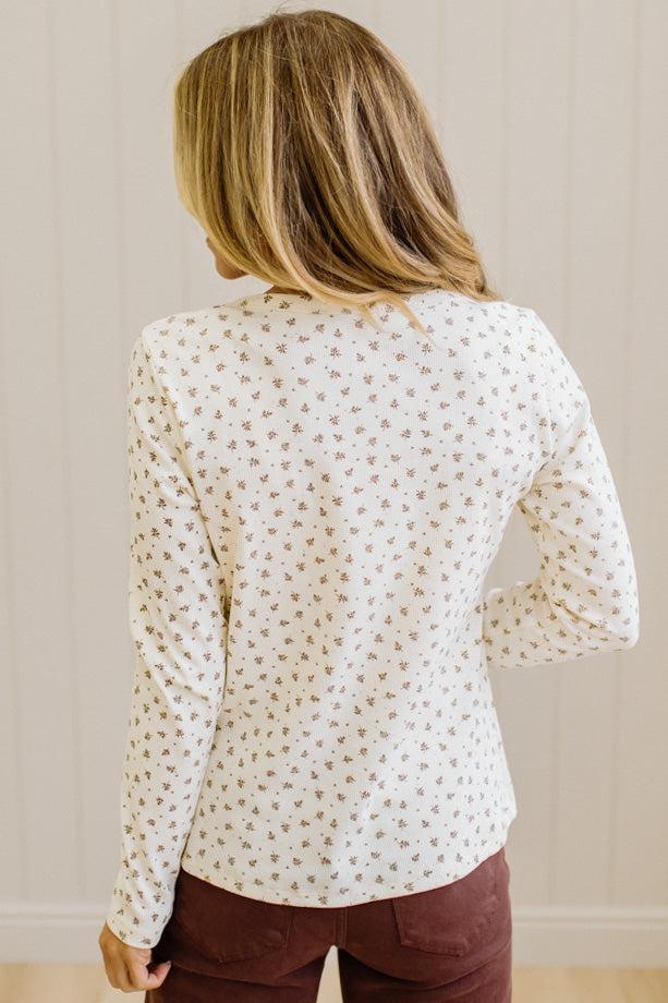 Blonde woman in brown jeans wearing a cream long sleeve tee with brown botanical print.