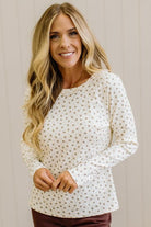 Blonde woman in brown jeans wearing a cream long sleeve tee with brown botanical print.