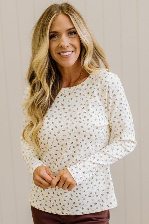 Blonde woman in brown jeans wearing a cream long sleeve tee with brown botanical print.
