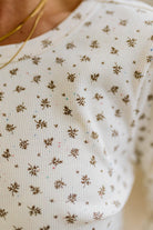 Blonde woman in brown jeans wearing a cream long sleeve tee with brown botanical print.
