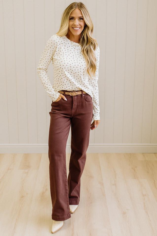 Blonde woman in brown jeans wearing a cream long sleeve tee with brown botanical print.