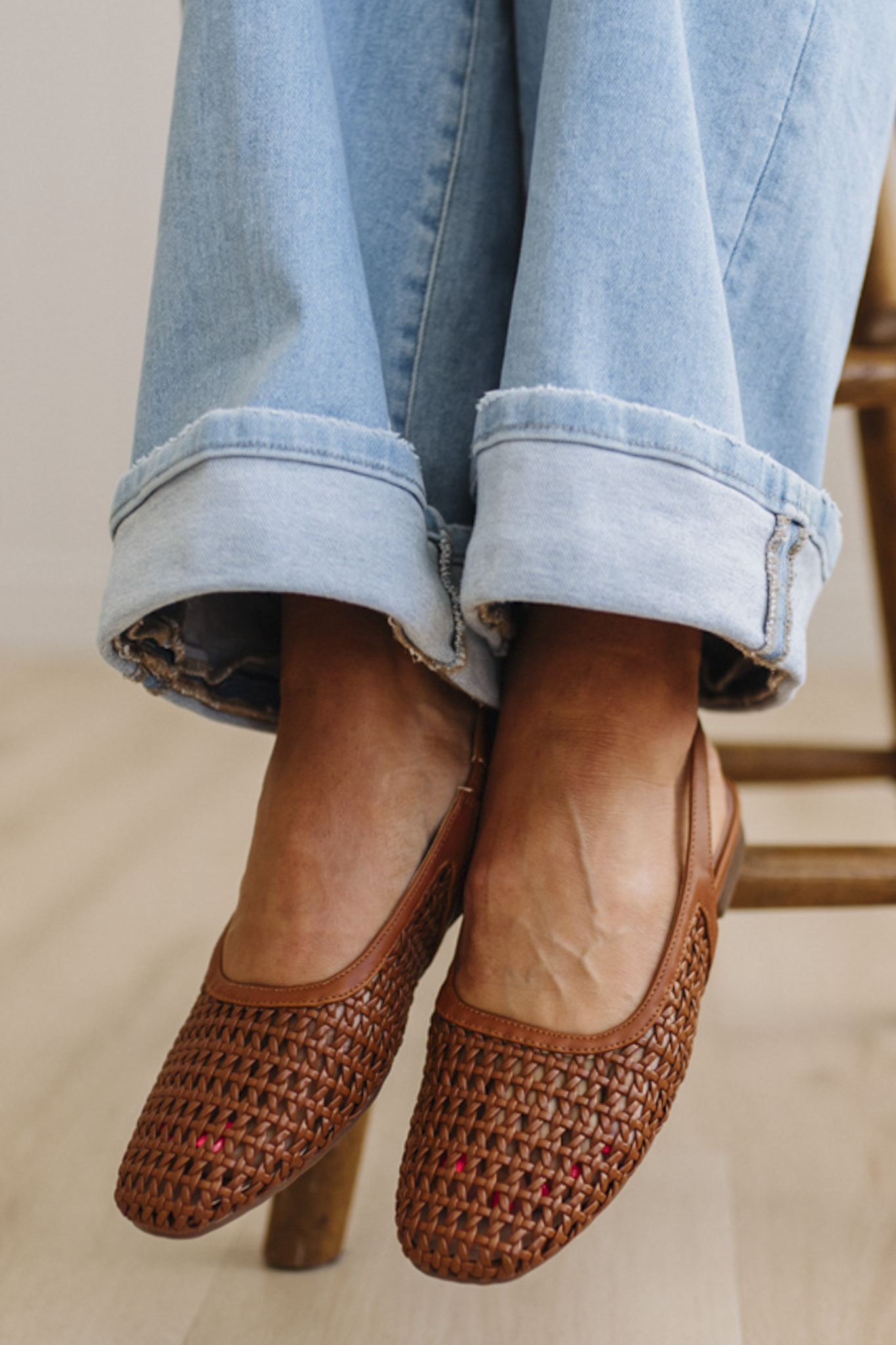 Brown woven shoes worn with light blue jeans on a neutral background