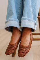 Brown woven shoes worn with light blue jeans on a neutral background