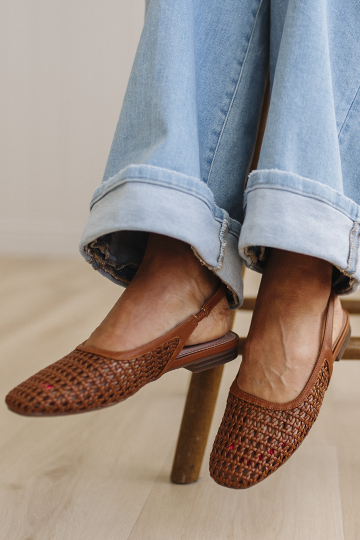 Brown woven shoes worn with light blue jeans on a wooden floor.