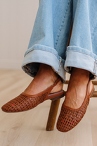 Brown woven shoes worn with light blue jeans on a wooden floor.