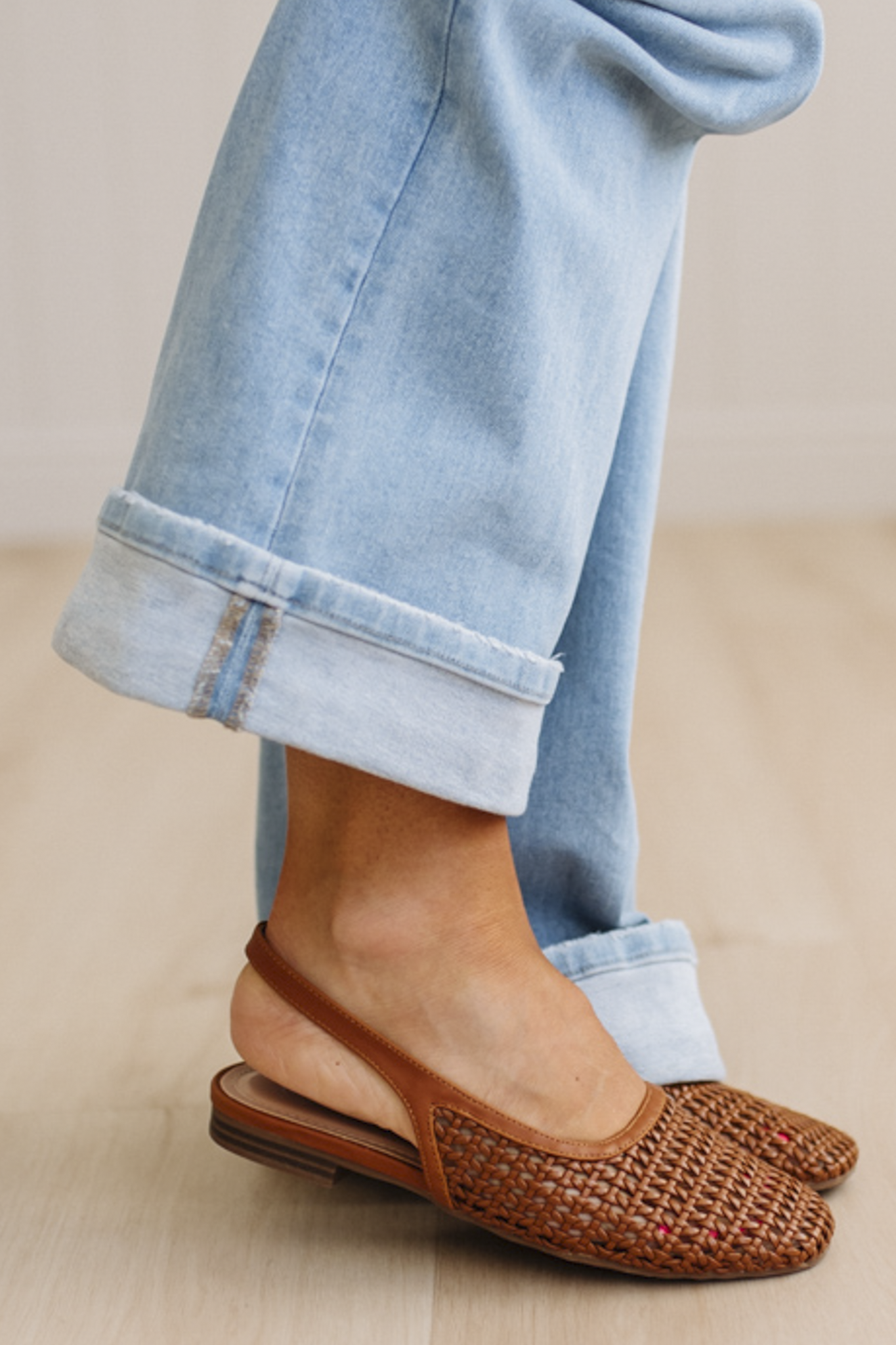 Brown woven flats worn with light blue jeans on a neutral background