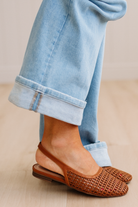 Brown woven flats worn with light blue jeans on a neutral background