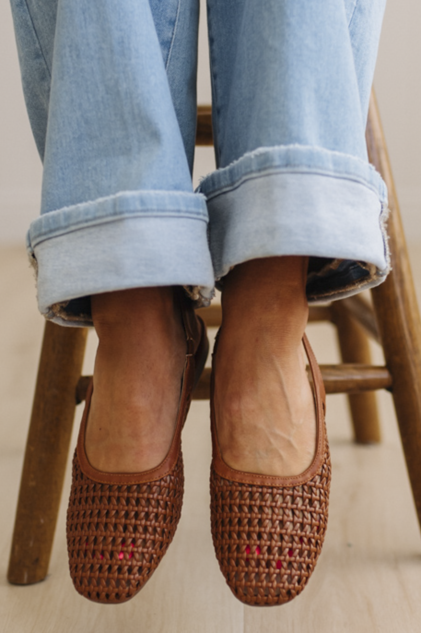 Brown woven flats worn with rolled-up jeans on a wooden chair.